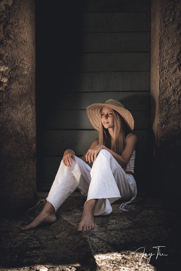 Girl with a straw hat is sitting in front of a door at an old mill in south france.