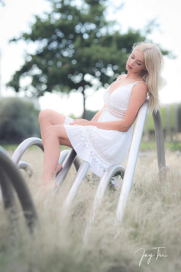 Teen Girl in white dress sitting on an sculpture.