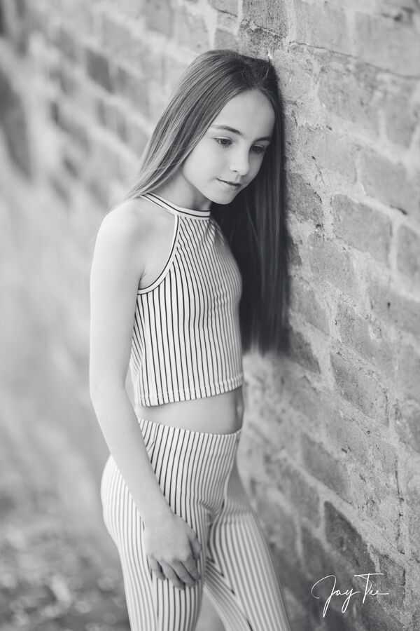 Girl in striped top and pants leans at wall.