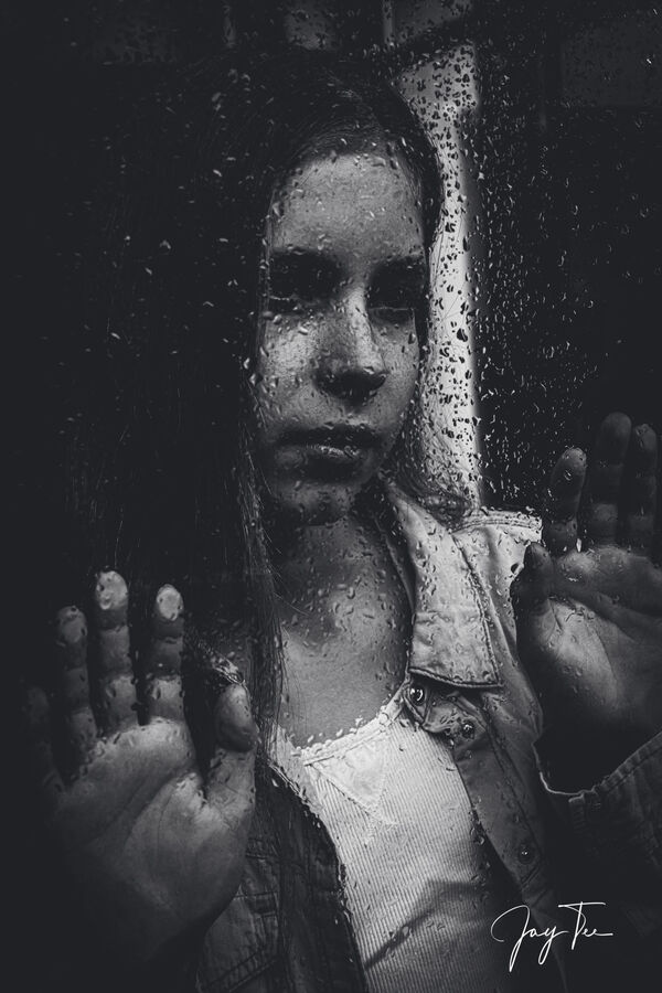 Teenager girl looks out of a window which is covered by rain drops.